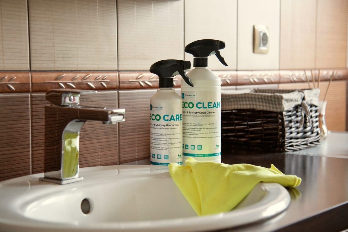 Eco-friendly cleaning products and a yellow microfibre cloth on a bathroom sink