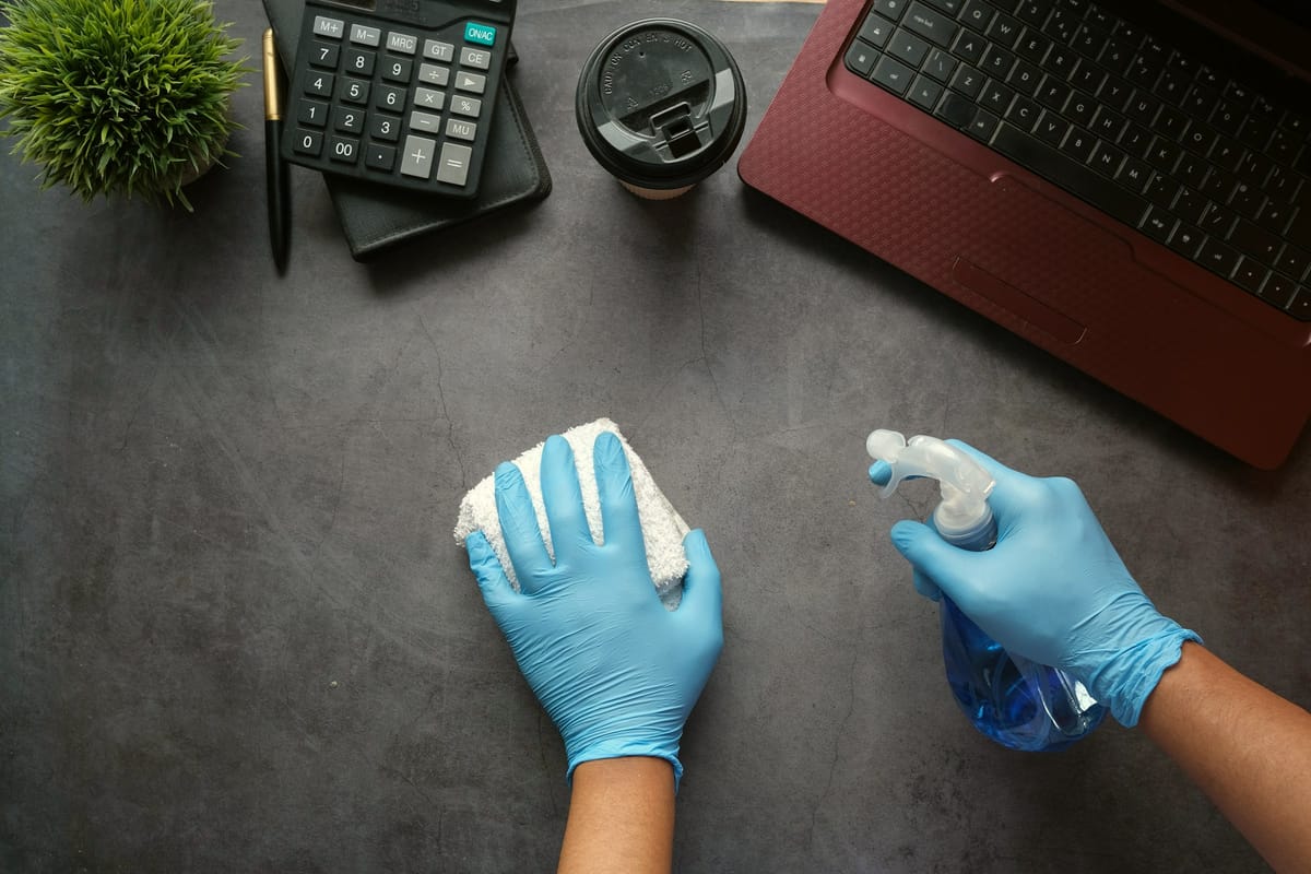 Cleaner in gloves disinfecting an office desk in Hamilton